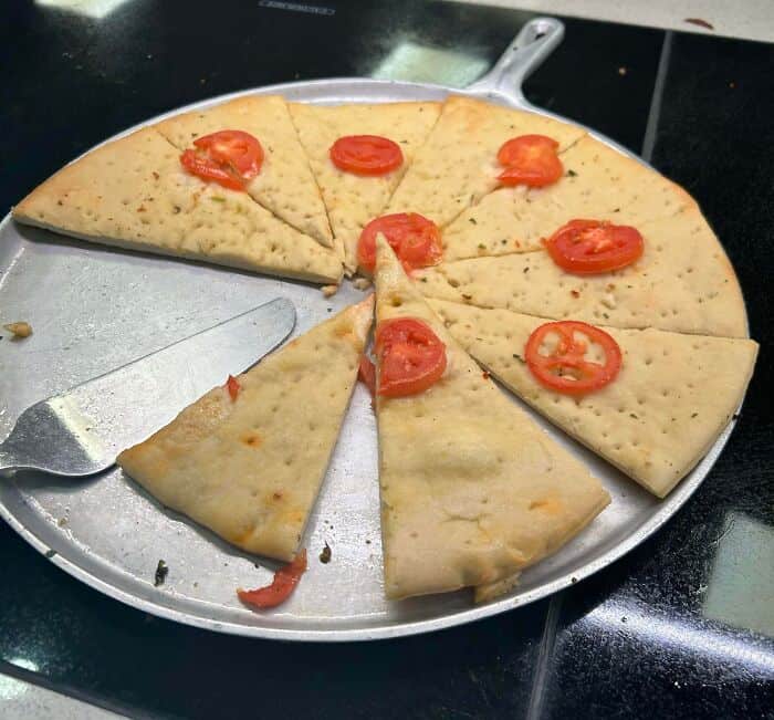 Cheese pizza with tomato slices on a round metal tray.
