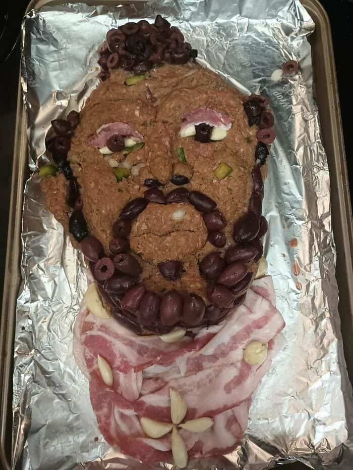 Face-shaped food made with ground meat, olives, and cheese on foil.