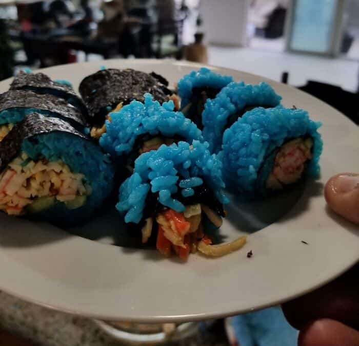 Blue sushi rolls with strange fillings, served on a white plate in a restaurant setting.