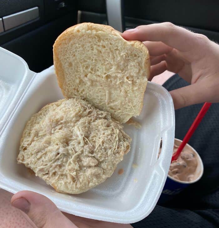 Unappealing chicken sandwich with bread and shredded meat in a foam container.