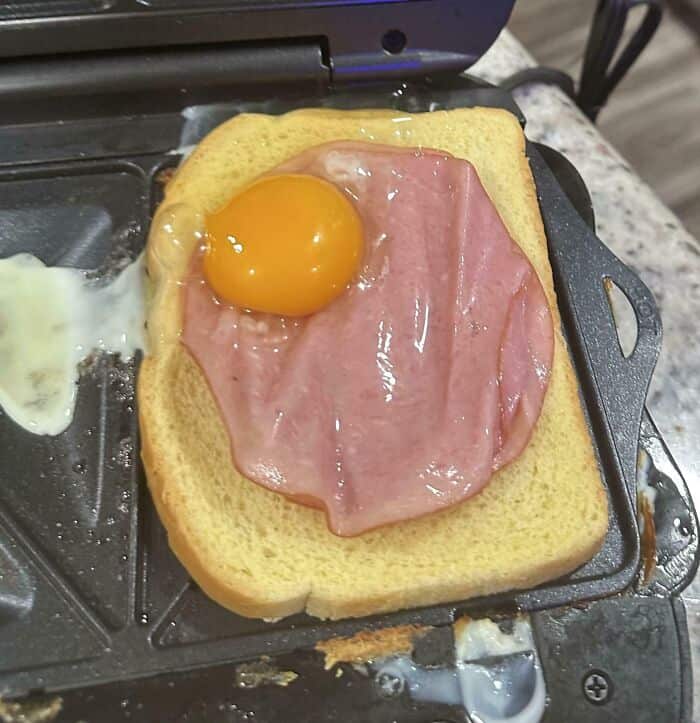 Egg and ham breakfast sandwich on bread, cooked on a griddle.