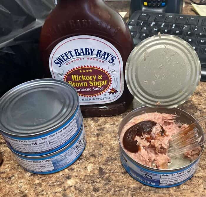 Opened can of tuna with BBQ sauce and a jar of sauce on a kitchen counter.
