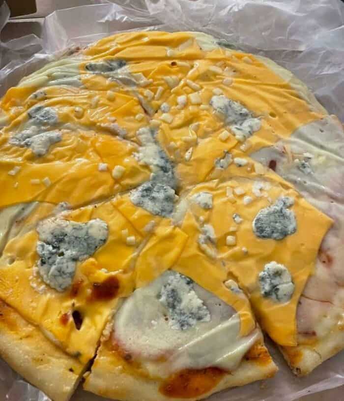Unusual pizza with blue cheese and yellow cheese toppings, creating a bizarre appearance.