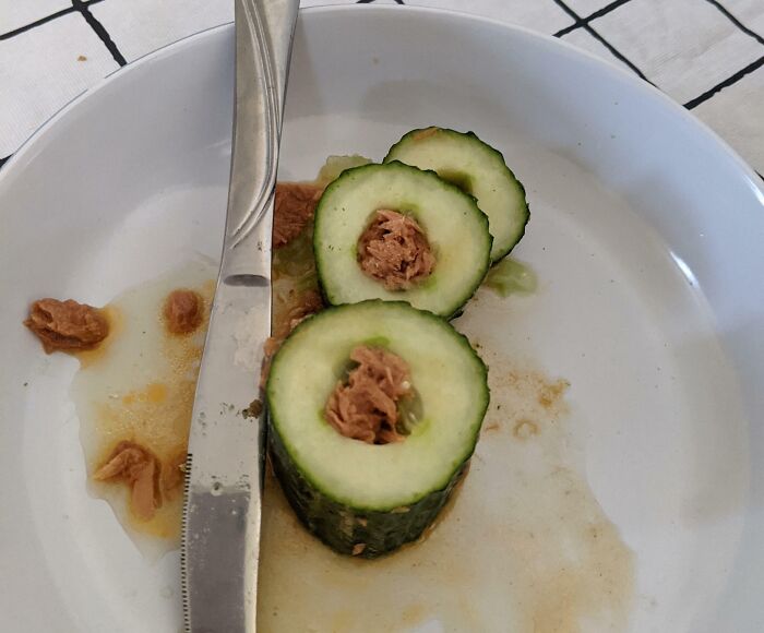 Cucumber slices filled with tuna, on a white plate with a knife.