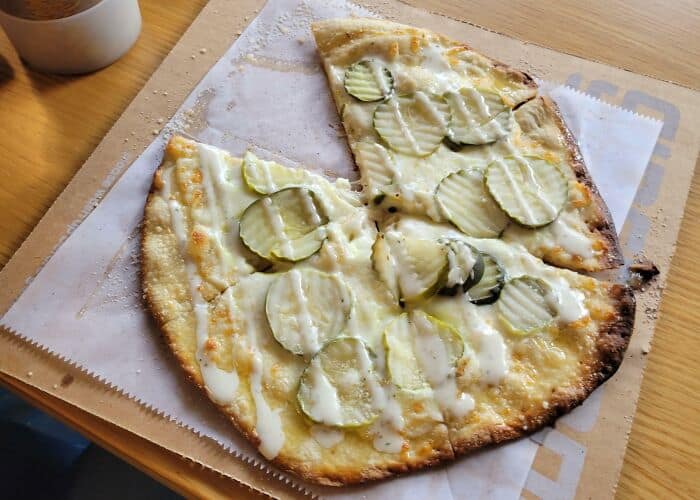 Unusual pickle and cheese pizza with melted cheese on a wooden table.