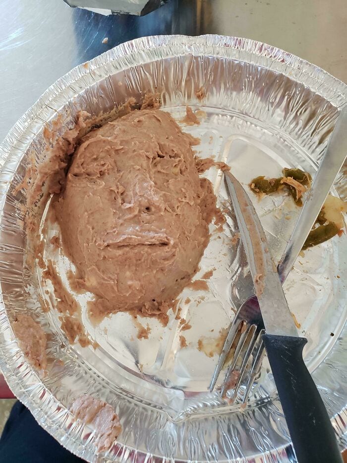 Unappealing canned meat in foil tray with fork and knife, labeled as cursed food.