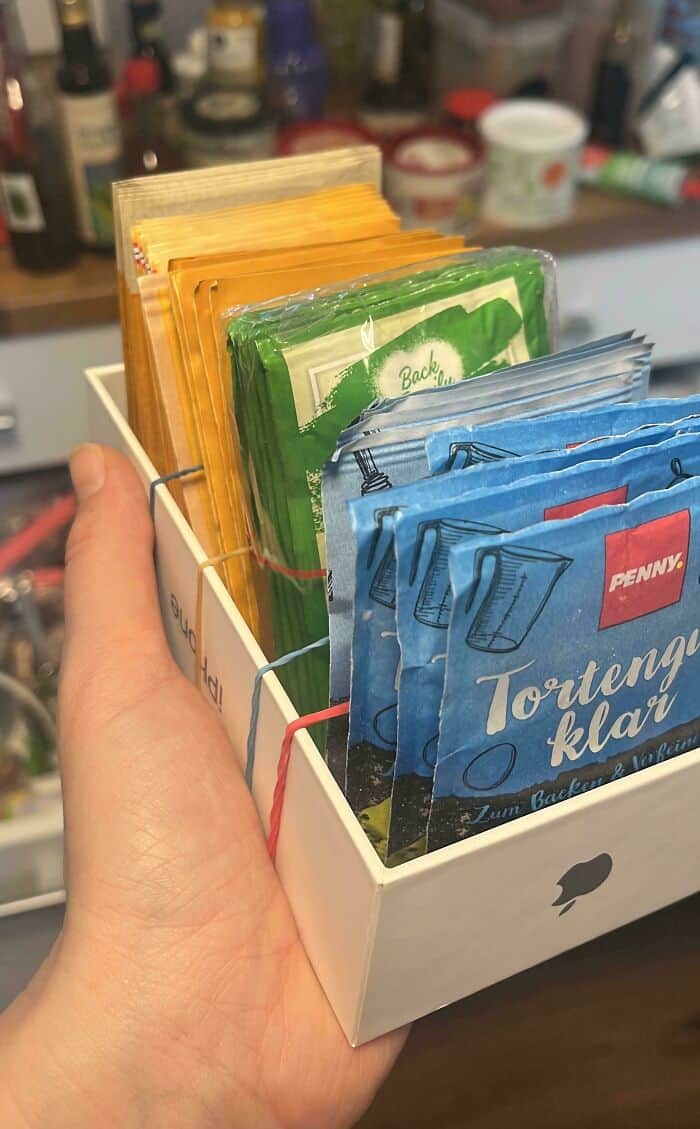 Hand holding a box of assorted tea bags, neatly organized by color and type.