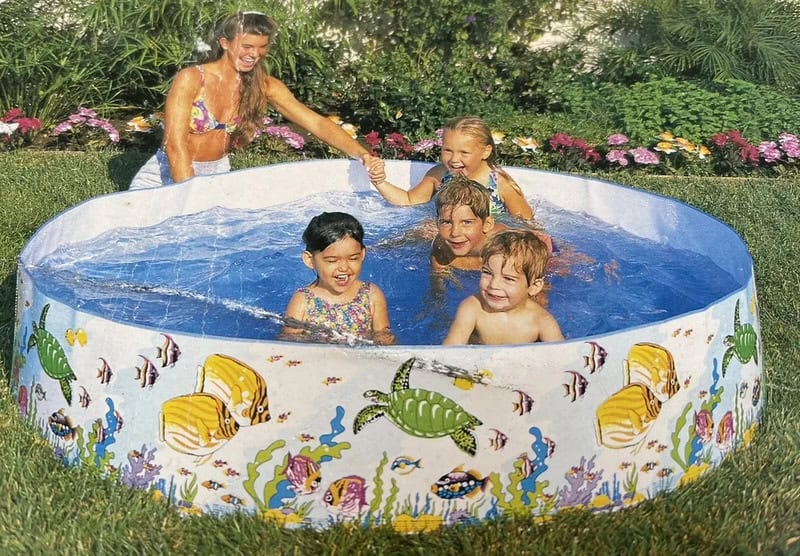 Children playing in a colorful inflatable pool with a woman, outdoors in a garden.