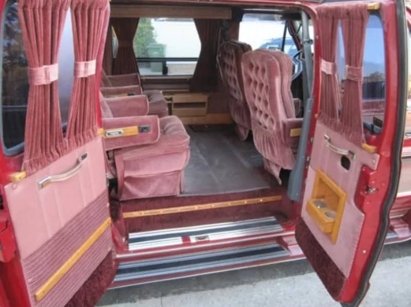Interior of a vintage pink bus with plush seats and curtains.