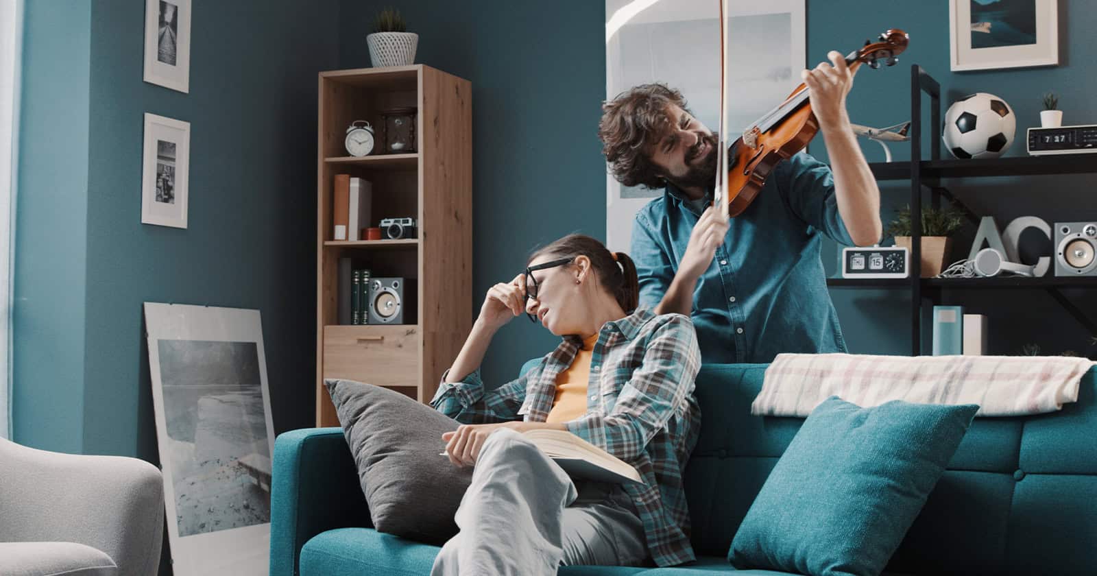 Two roommates relaxing in a living room, one playing guitar, the other reading.