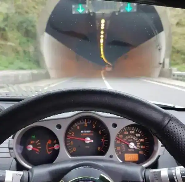 Driving through a tunnel with dashboard view and green directional signs above the road.