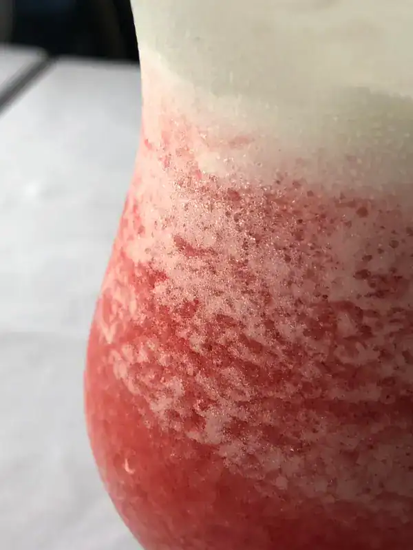 Pink and white layered beverage in a glass with a frosty appearance.