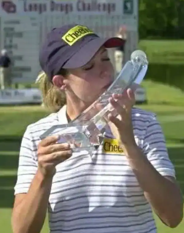 Woman kissing a large glass trophy at a golf course.