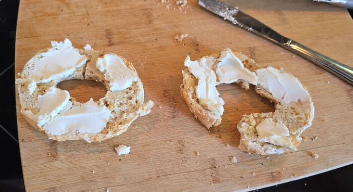 Bagel with cream cheese on a wooden cutting board.