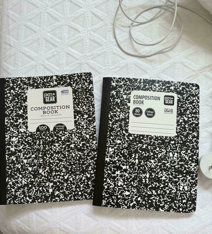 Two composition notebooks on a white textured surface with cords nearby.