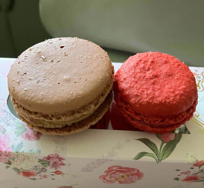 Cream-colored macaron with a smooth top and a red macaron with a textured top on a floral-patterned.