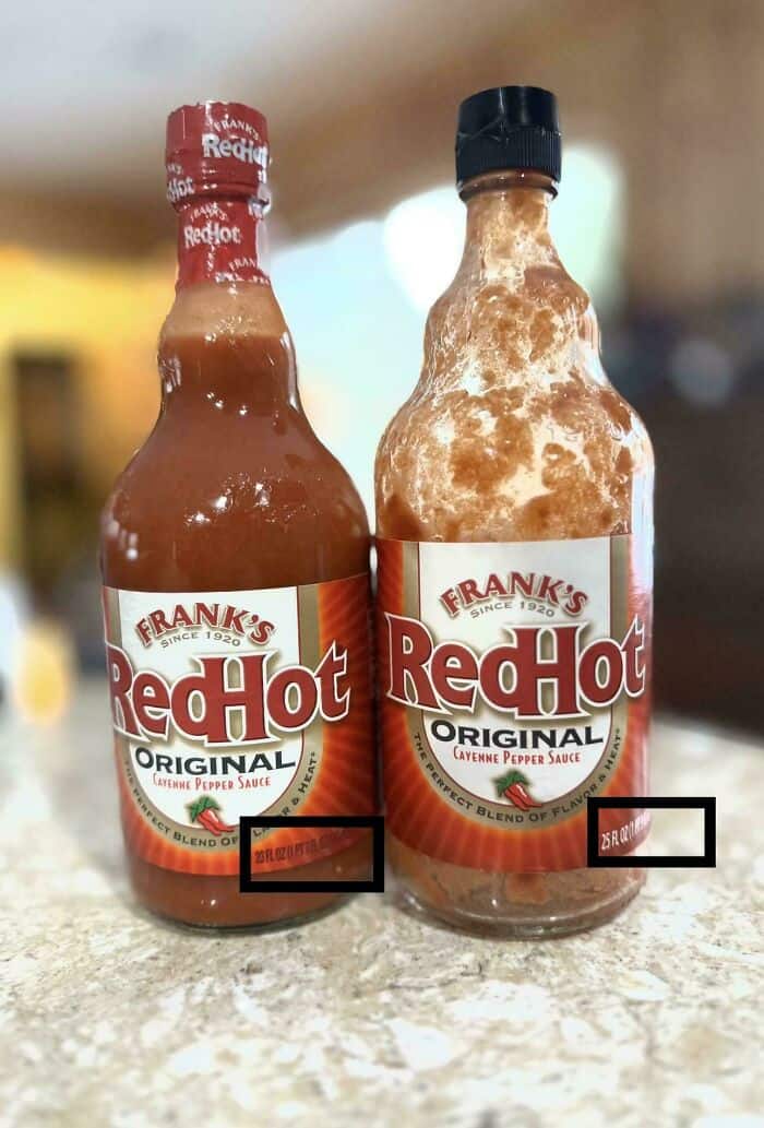 RedHot Original hot sauce bottles with one covered in sauce splatters, on a kitchen countertop.