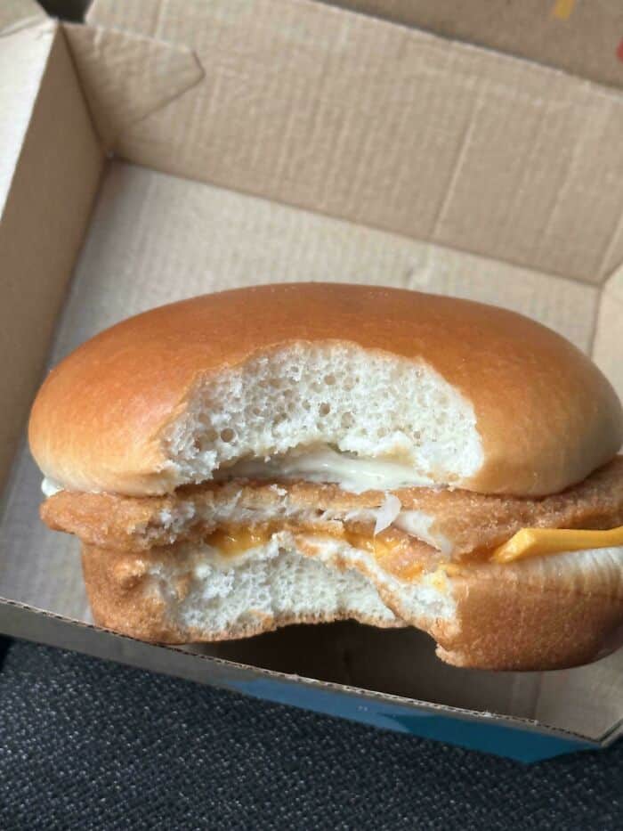 Sandwich with fried chicken fillet and melted cheese in a bun, inside a cardboard box.