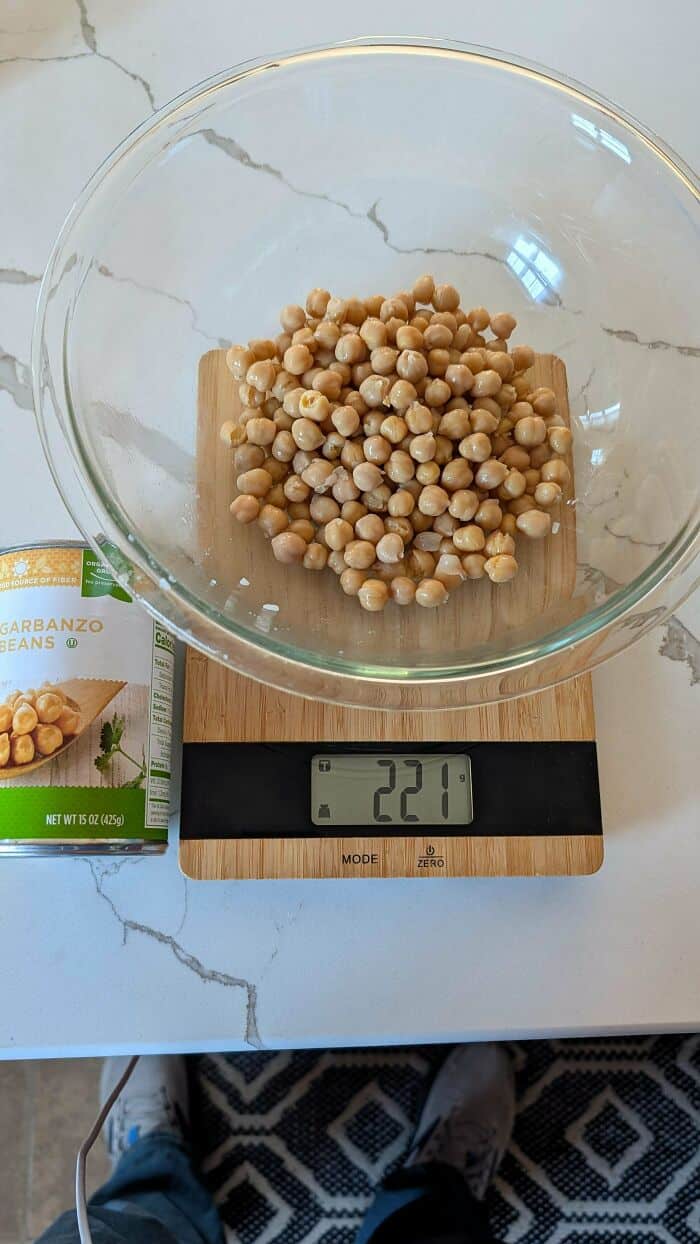 Roasted chickpeas in a glass bowl on a digital kitchen scale showing 221 grams.