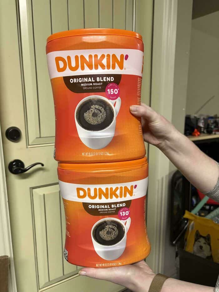Dunkin' Original Blend coffee containers, medium and dark roast, held by hands in front of a cabinet.