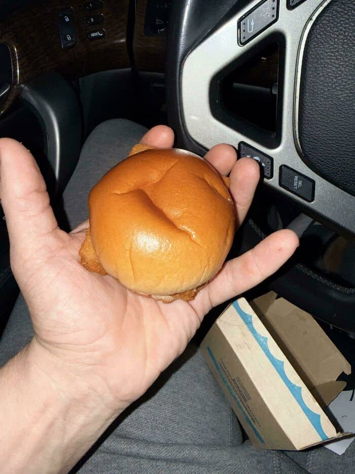 Hand holding a burger bun inside a vehicle.