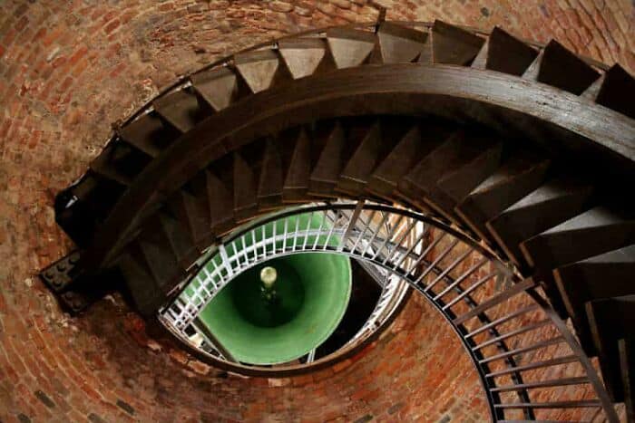 A spiral staircase with a green eye-shaped opening at the center, viewed from above.