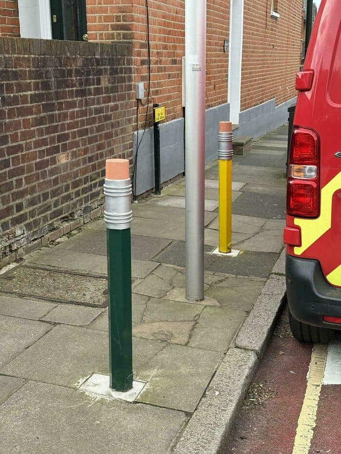 Street bollards and a parked red vehicle on a sidewalk.