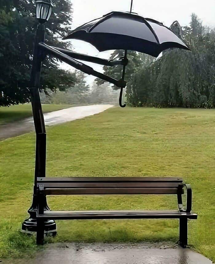 An umbrella attached to a park bench in the rain.