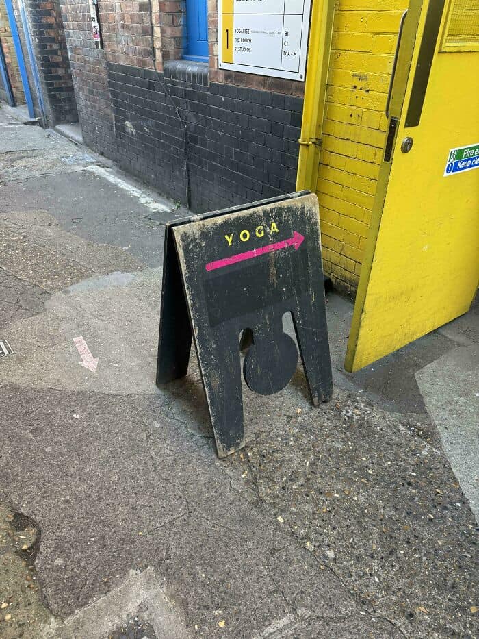 YOGA signboard on sidewalk near yellow building and black brick wall.