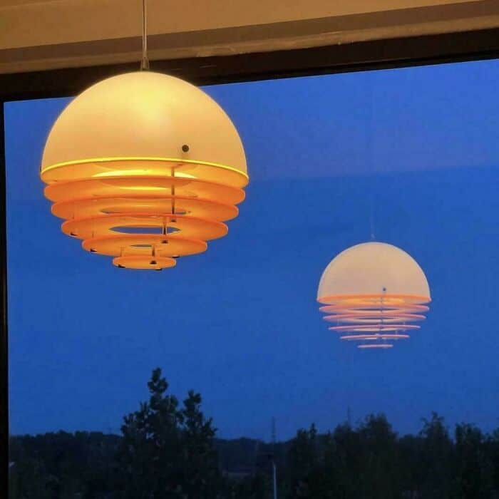 Warm yellow and white hanging lamps glowing against a blue evening sky with trees in the background.