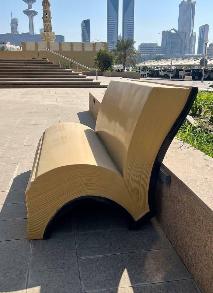 Unique bench designed to look like an open book in an urban setting with skyscrapers in the backgrou.