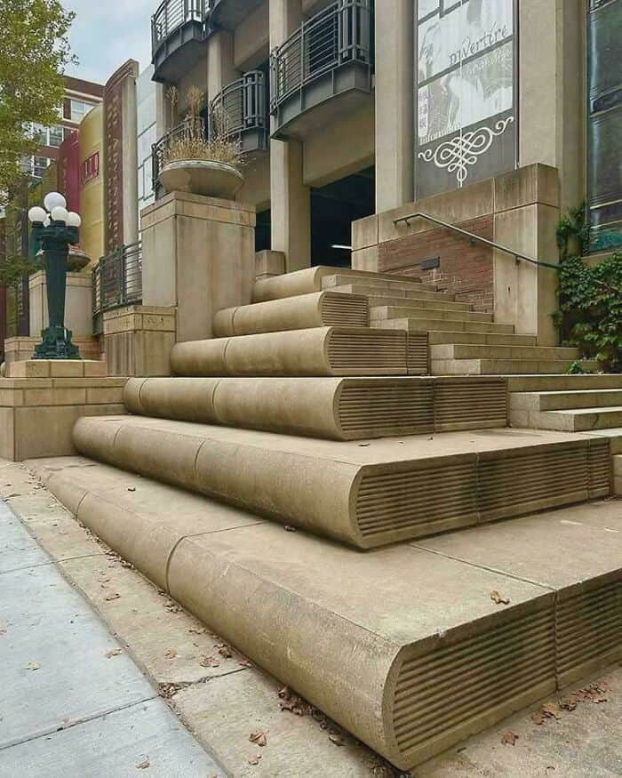 Stairs with rounded, ribbed design leading up to a building entrance, with a lamp post nearby.