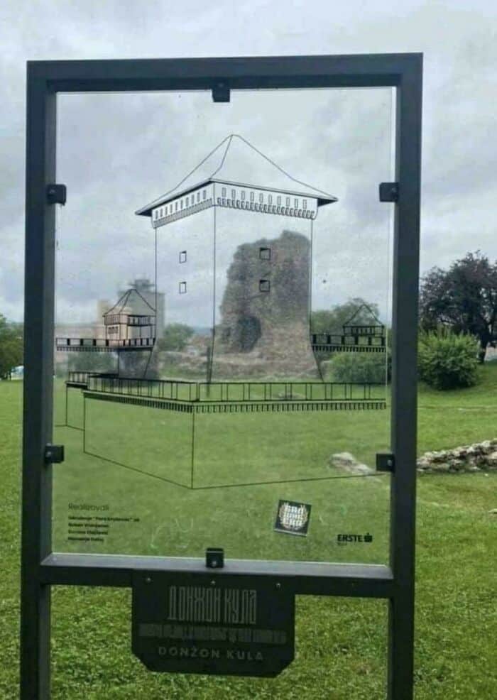 Ancient stone tower with modern glass display and surrounding greenery.
