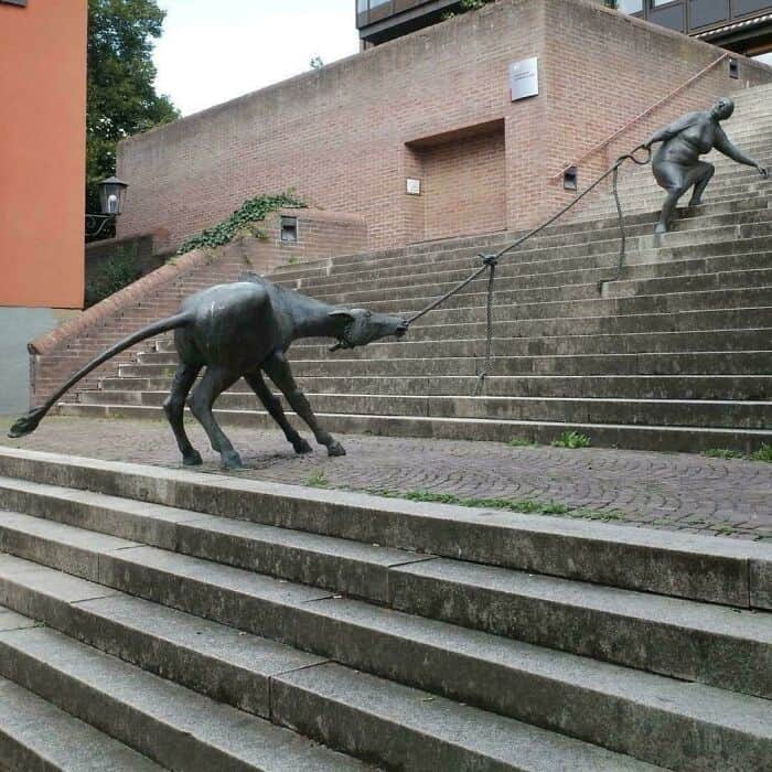 Sculpture of a dog pulling a person up stairs with a leash.