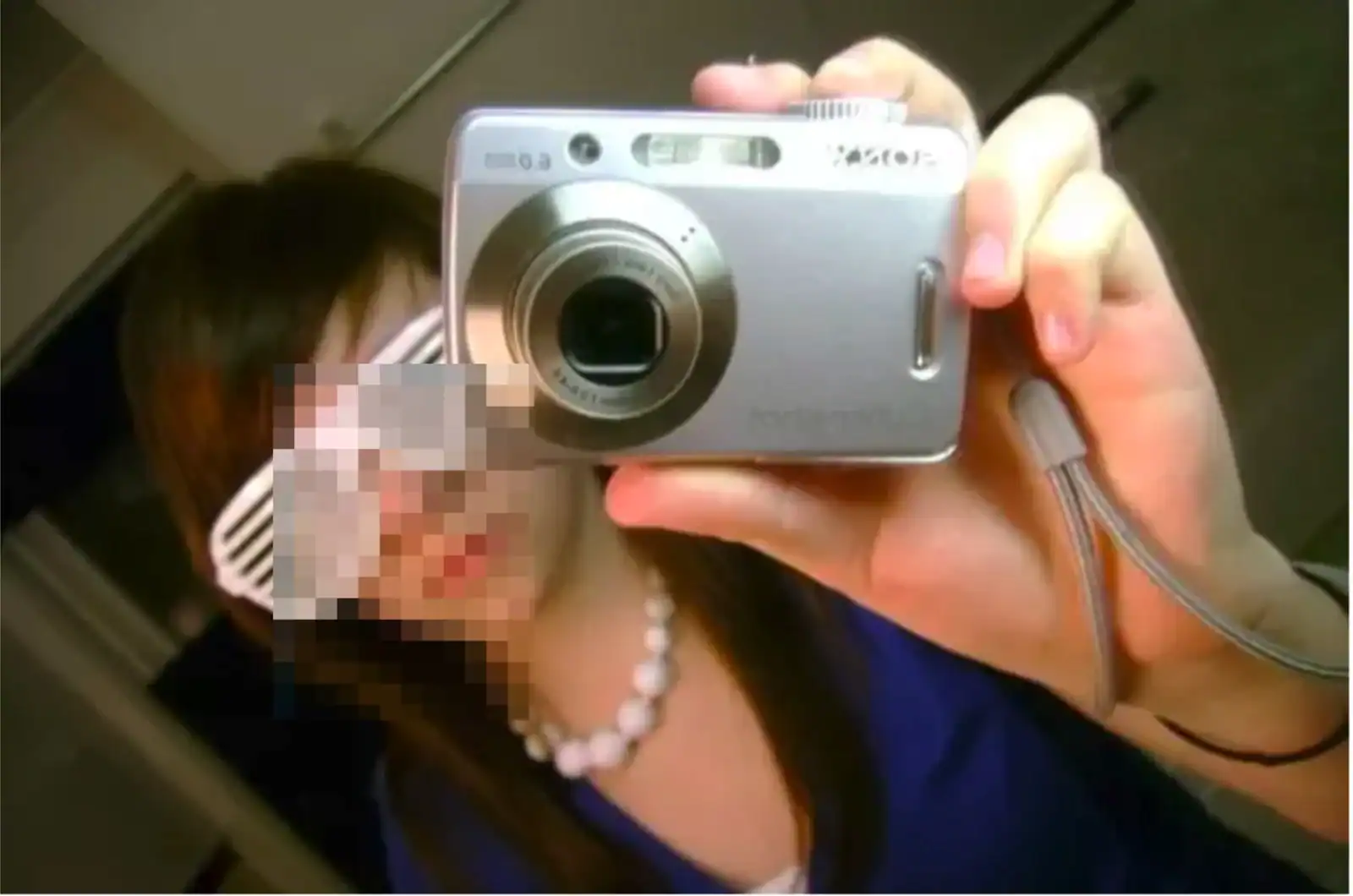 Selfie of a woman taking a photo with a digital camera, wearing a blue top and pearl necklace, in an.