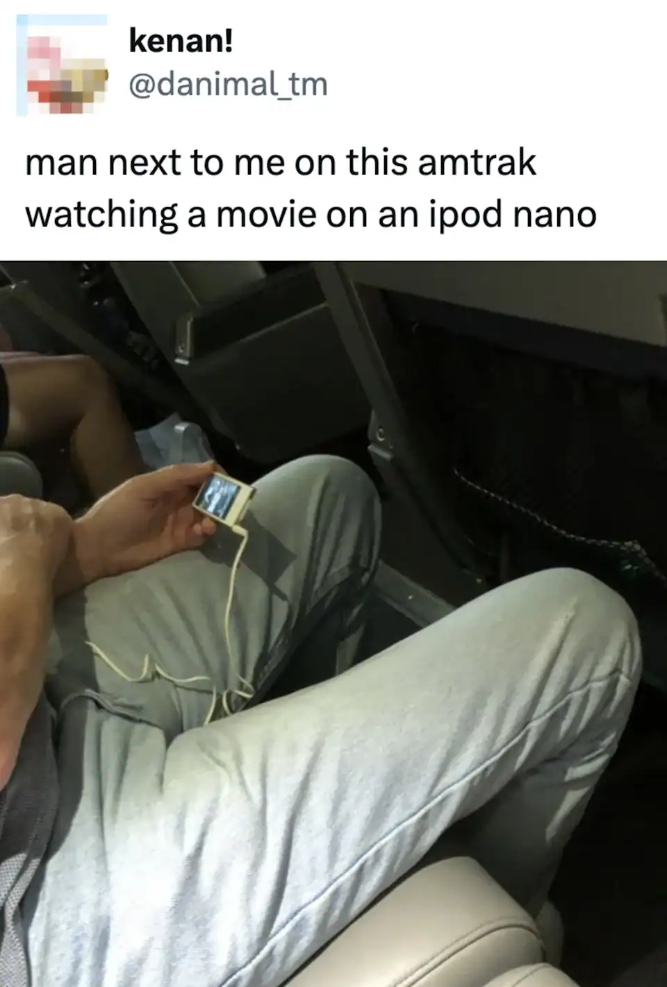 Man sitting on Amtrak train, watching a movie on an iPod Nano, with headphones, wearing light-colore.