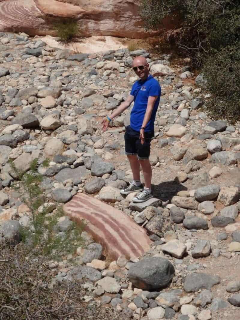 Man standing on rocky desert landscape with a large striped rock in the foreground.