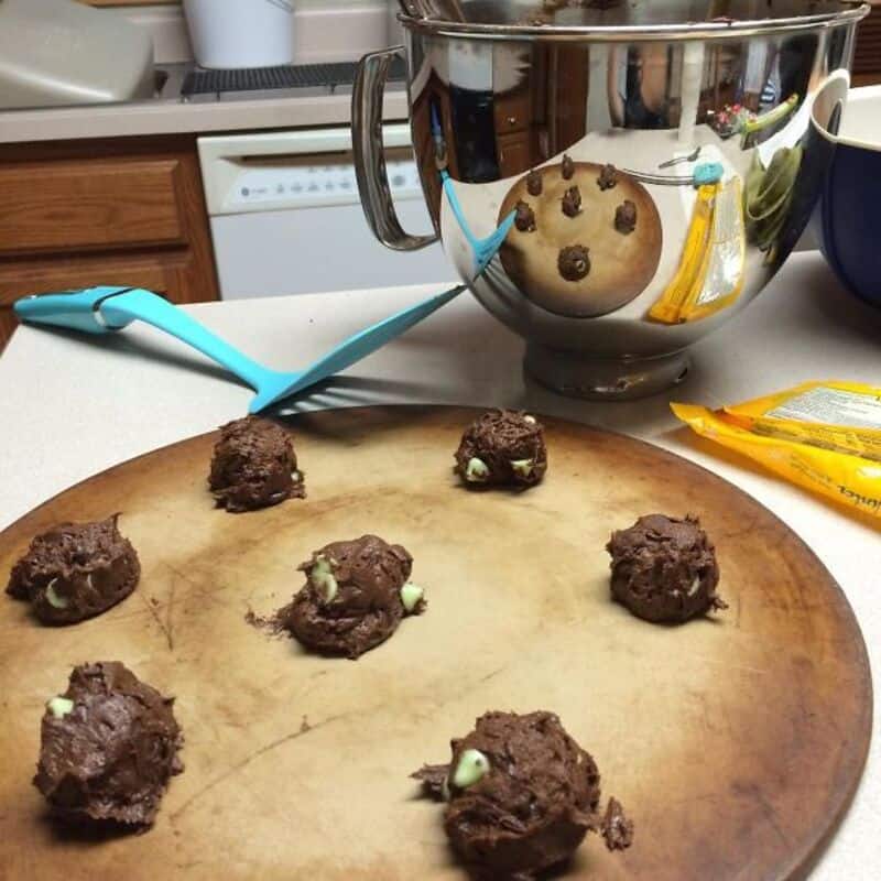 Freshly made chocolate chip cookie dough bites on a wooden cutting board in a kitchen setting.