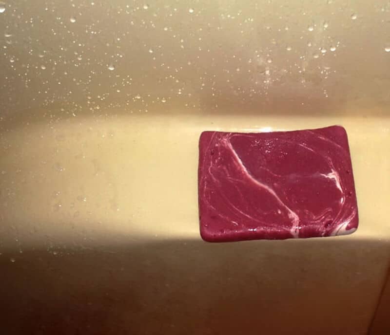 Red marbled soap bar resting on a metallic surface with water droplets.