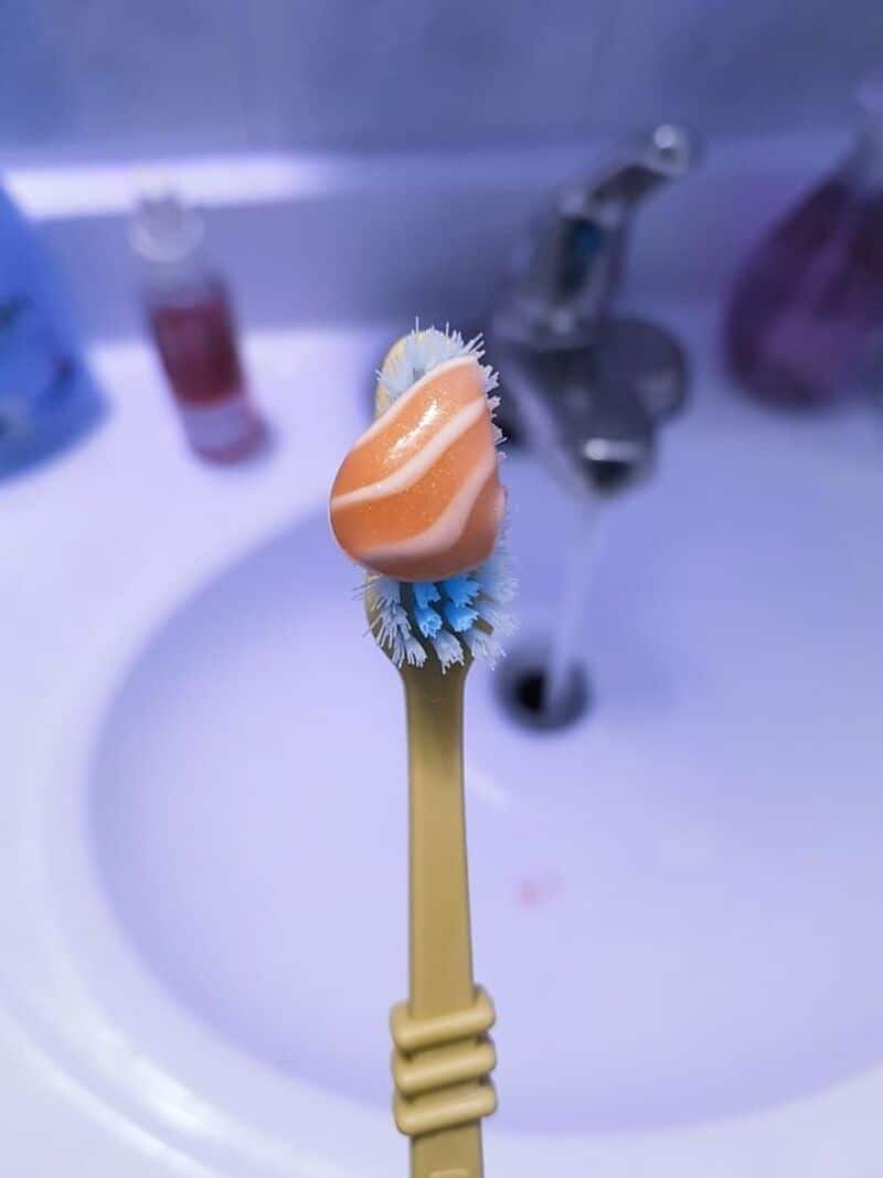 Close-up of a toothbrush with soap foam on bristles over bathroom sink.