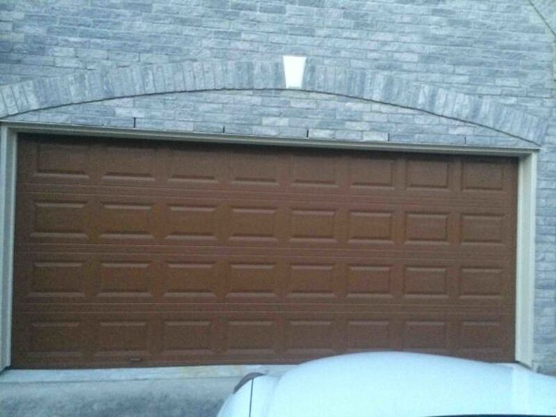 Garage door with brick archway and white light above, part of a residential home exterior.