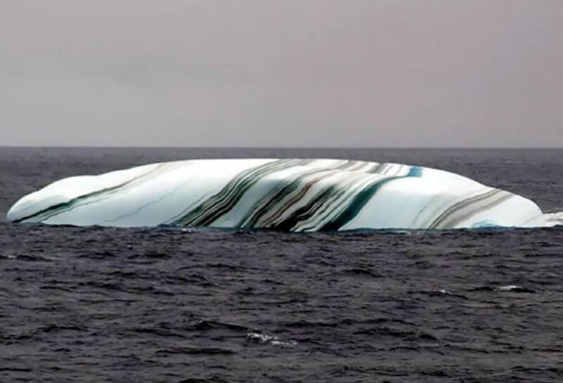 Large iceberg with black and white striped patterns floating in the ocean.