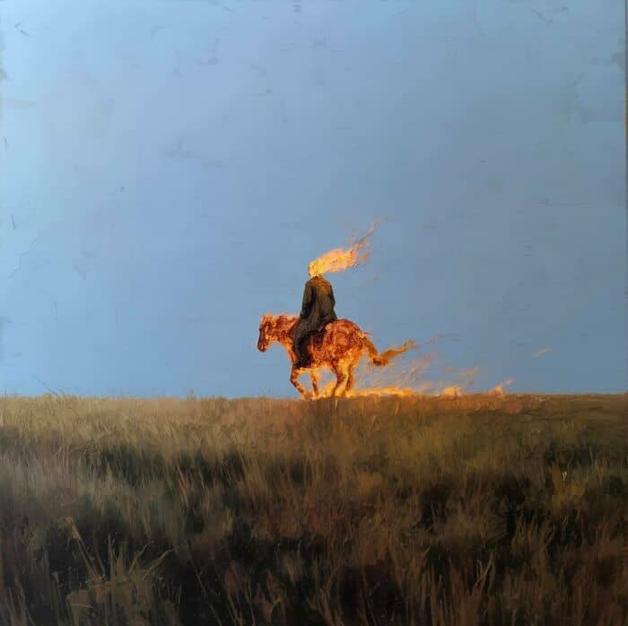 Horse with a flaming mane standing in a grassy field under a blue sky.