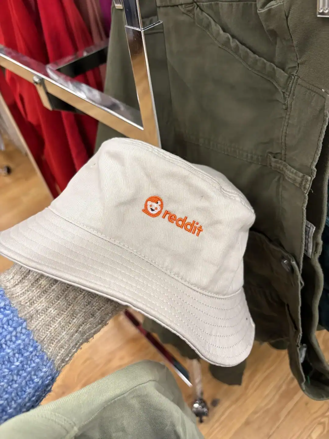 Reddit logo bucket hat displayed among thrift store clothing items, showcasing unique vintage fashio.