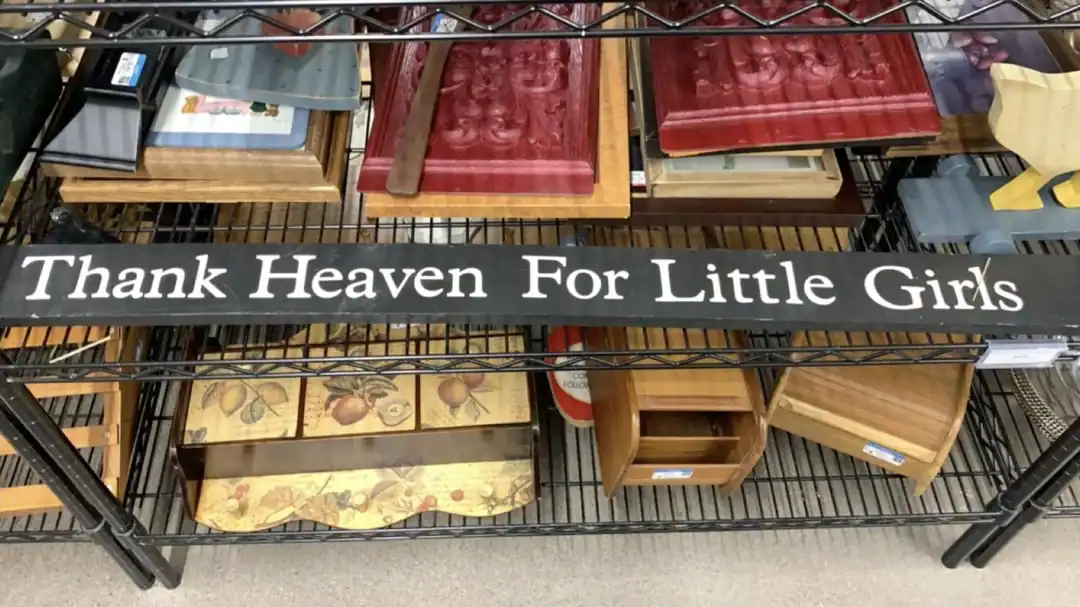 Vintage wooden bookshelf displaying decorative books and a "Thank Heaven For Little Girls" sign.