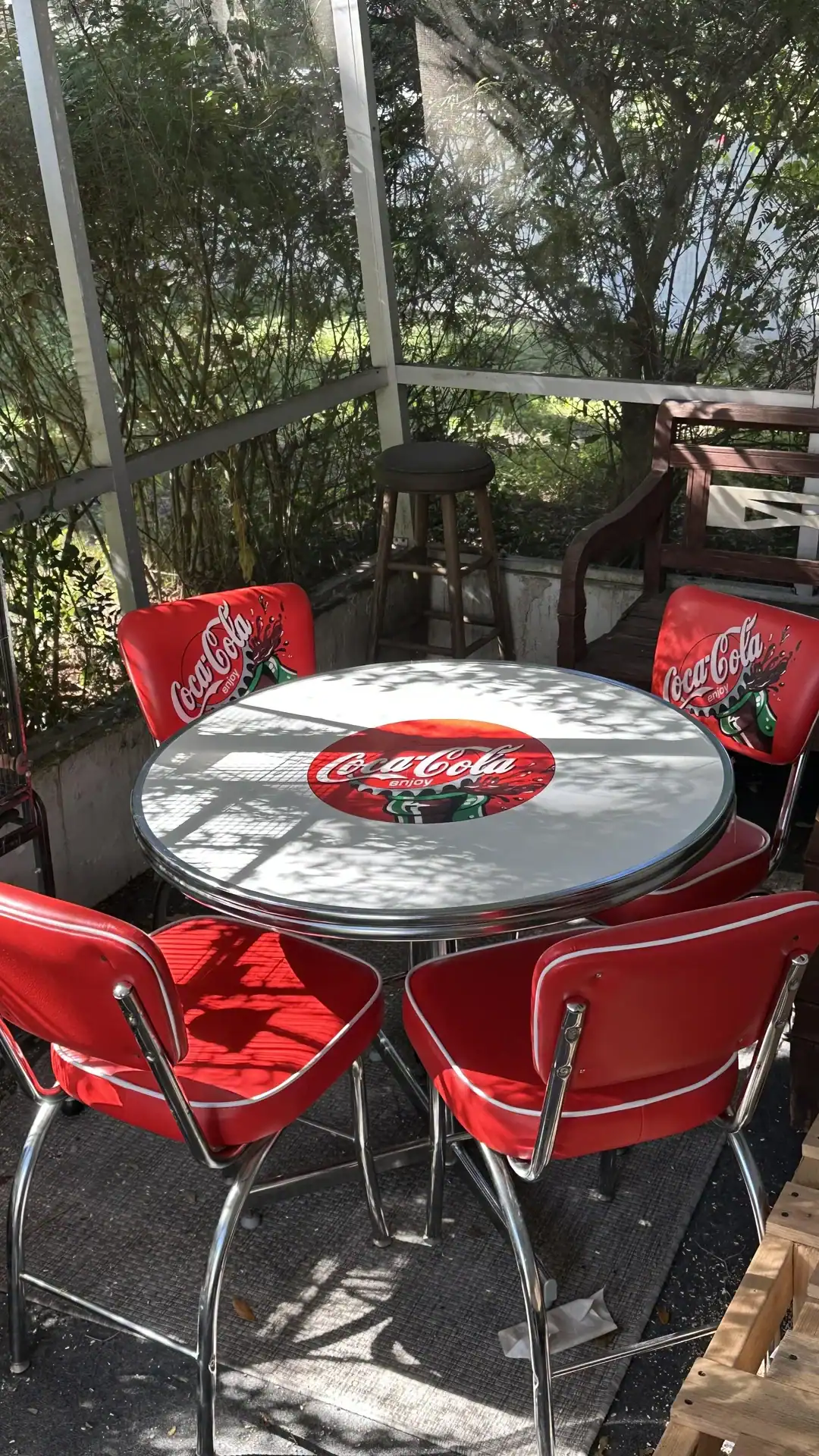 Vintage Coca-Cola themed outdoor table with red chairs on a screened porch.