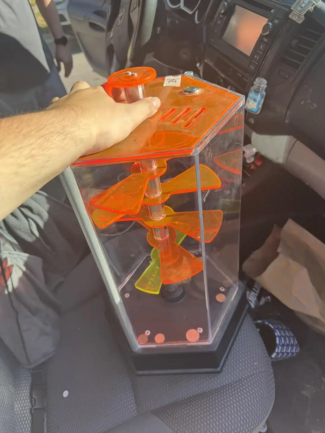 Vintage orange plastic toy propeller in a clear display case, inside a vehicle.