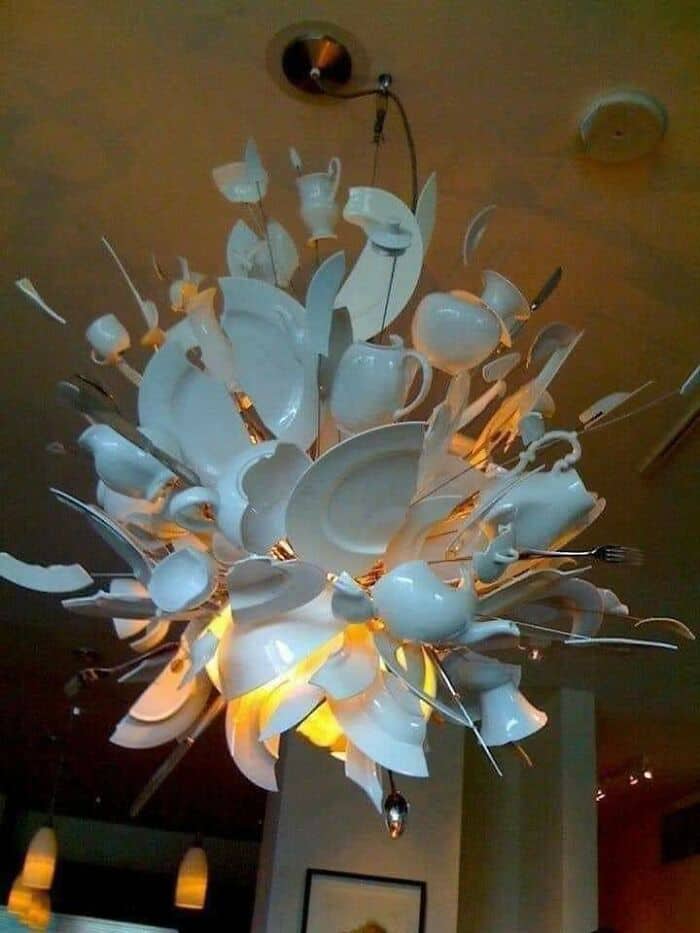 Unique chandelier made from broken white plates and utensils, creating an artistic lighting fixture.