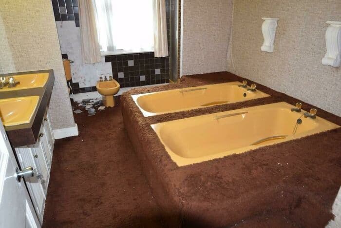 Vintage bathroom featuring two built-in bathtubs, brown carpeting, and classic wall-mounted fixtures.