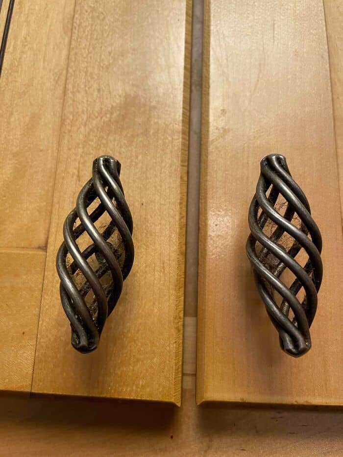 Decorative twisted metal cabinet handles on wooden drawers.